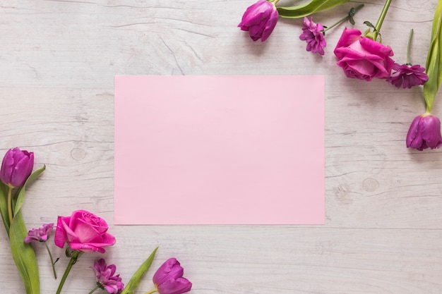 Flores cor de rosa com papel na mesa de madeira