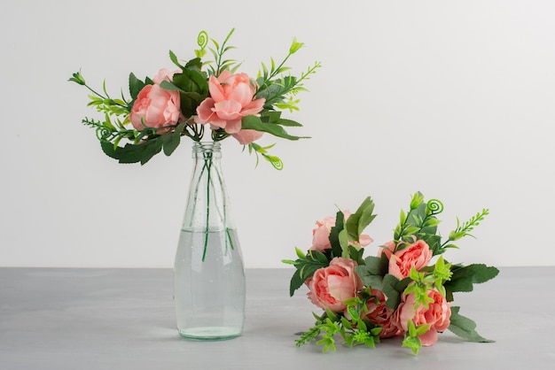 Flores cor de rosa em um vaso de vidro e buquê de flores na mesa cinza