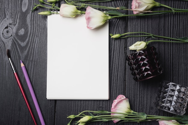 Flores frescas com papel branco em branco com lápis colorido e pincel na mesa de madeira preta