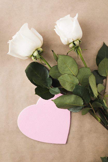 Foto grátis flores rosas com coração de papel na mesa bege