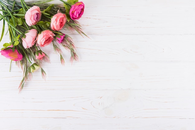 Flores rosas cor de rosa com ramos de plantas na mesa de madeira