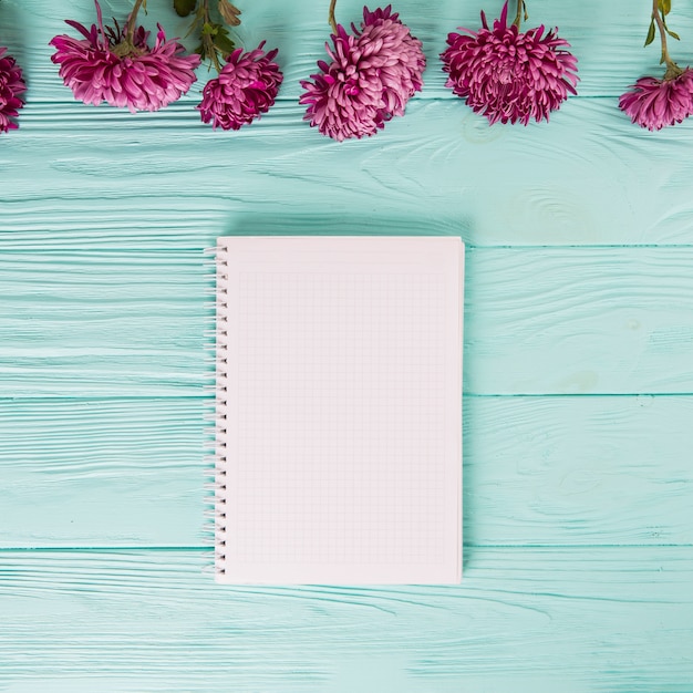 Flores roxas com um caderno em branco na mesa azul