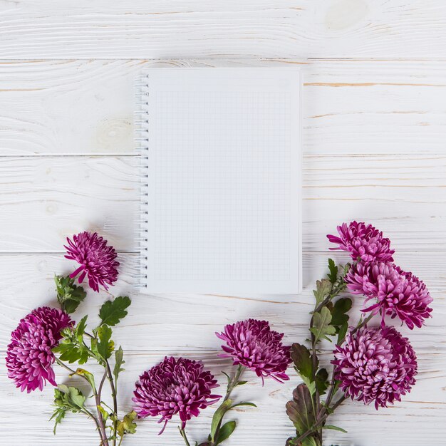 Flores roxas com um caderno em branco na mesa de madeira