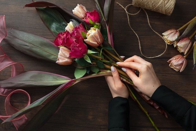 Florista no trabalho: mulher fazendo moda buquê moderno de flores diferentes na superfície de madeira.