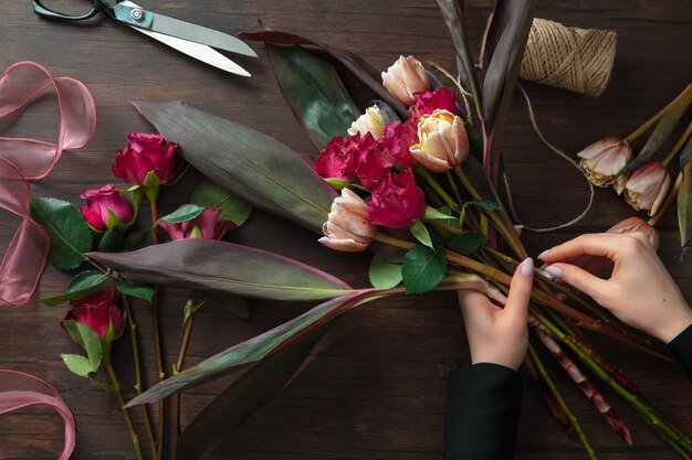 Florista trabalhando, mulher fazendo buquê moderno de flores diferentes na superfície de madeira