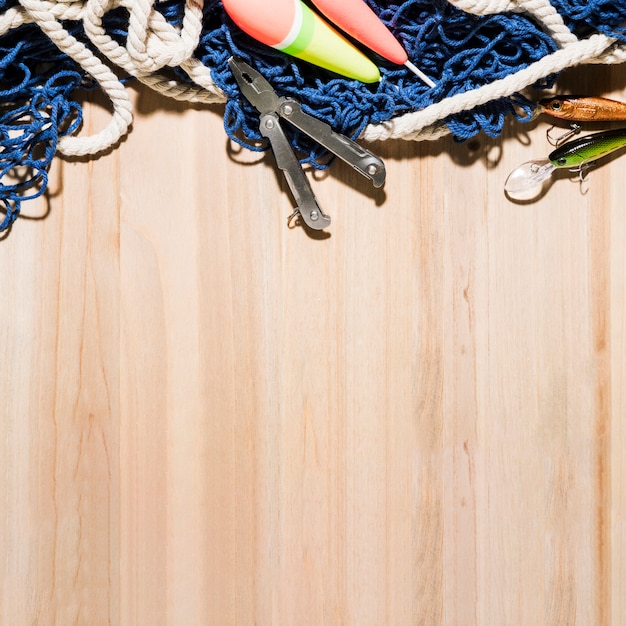 Foto grátis flutuador de pesca; alicate; isca de pesca e rede de pesca na superfície de madeira