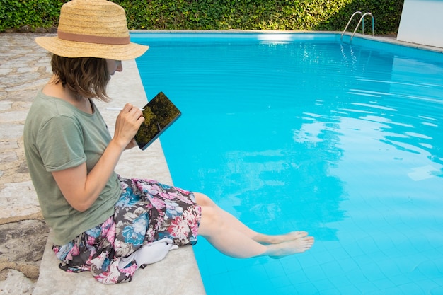 Focada mulher de chapéu de palha sentado à beira da piscina