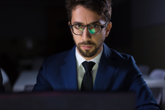 Foco homem sentado à mesa com o laptop e olhando para a câmera