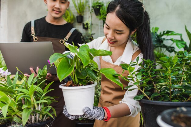 Foco seletivo, jovem casal de jardineiros asiáticos vestindo avental usa equipamento de jardim e um laptop para cuidar