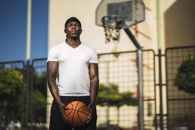 Foto grátis foco superficial de um homem afro-americano de camisa branca em pé na quadra de basquete