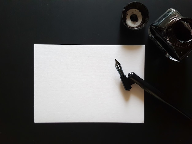 Folha de papel, caneta e tinta de preto na mesa de escritório preto.