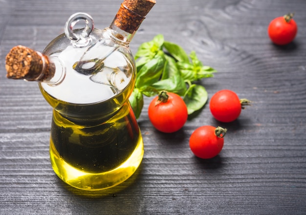 Folhas de manjericão; tomates e garrafa de azeite com rolha de cortiça