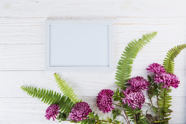 Folhas de samambaia verde com flores roxas e moldura na mesa