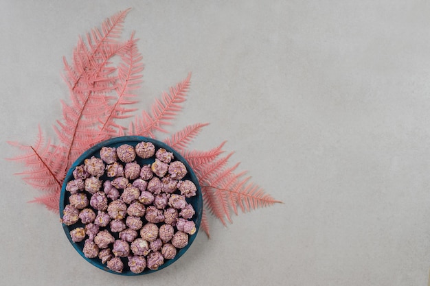Folhas decorativas debaixo de uma tigela de doces pipoca no fundo de mármore.