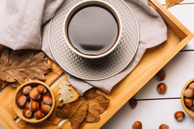 Folhas e nozes perto de café na bandeja