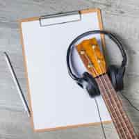 Foto grátis fone de ouvido sobre o cabeçote de guitarra sobre o papel branco na prancheta com lápis