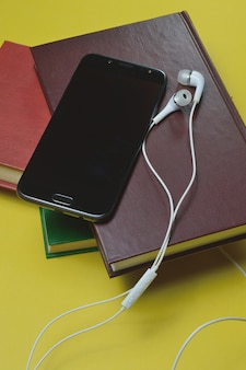 Fones de ouvido com livros e um smartphone em um fundo amarelo.