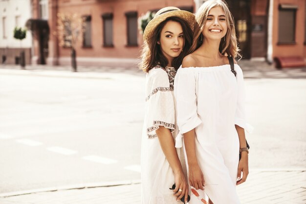 Forme o retrato de dois modelos de mulheres jovens loiras e morenas hippie elegante em dia ensolarado de verão em hipster branco roupas posando. sem maquiagem