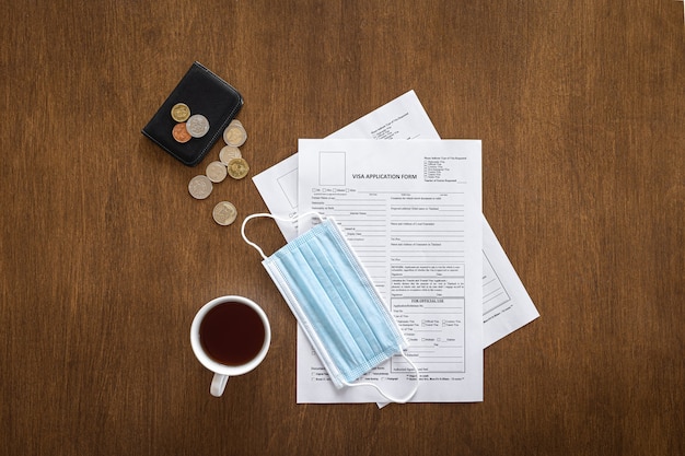 Foto grátis formulário de pedido de visto em uma mesa de madeira, máscara médica, dinheiro, vista superior, postura plana, processamento de visto, documentação, imigração.