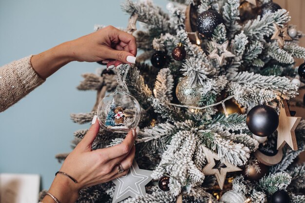 Foro recortado de mãos de senhora segurando um lindo brinquedo de veado perto da árvore de Natal. Conceito de véspera de ano novo
