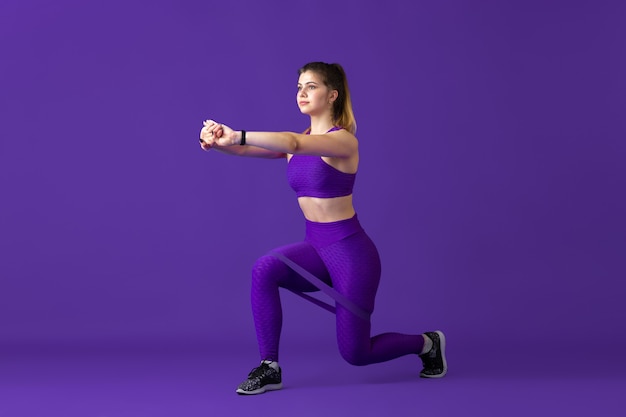 Forte. bela jovem atleta praticando, retrato roxo monocromático. modelo de ajuste caucasiano desportivo com elásticos. musculação, estilo de vida saudável, conceito de beleza e ação.