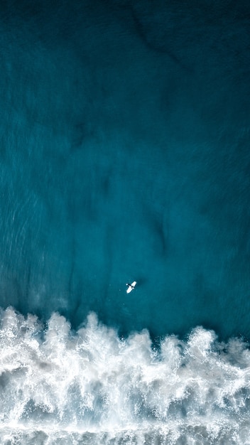 Foto aérea aérea vertical das belas ondas do mar com um avião voando acima