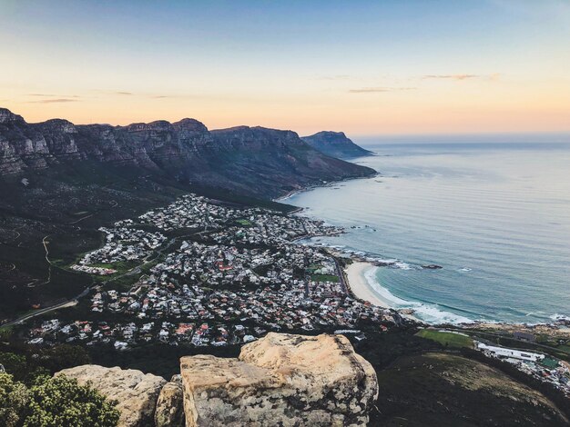 Foto aérea ampla de casas na costa do mar, rodeada por montanhas, sob um céu azul e rosa