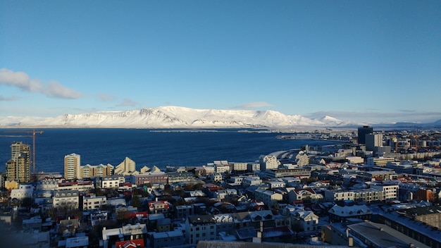 Foto aérea da cidade costeira de Reykjavik com montanhas cobertas de neve em um céu azul