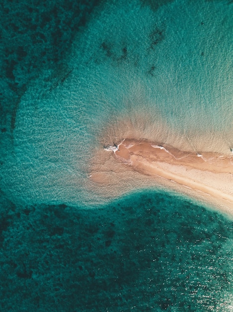 Foto aérea das ondas do mar atingindo a pequena ilha de areia