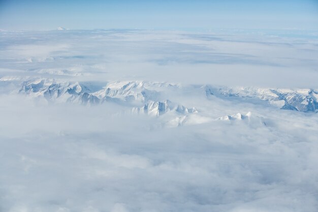 Foto aérea de tirar o fôlego do topo de montanhas nevadas cobertas de nuvens