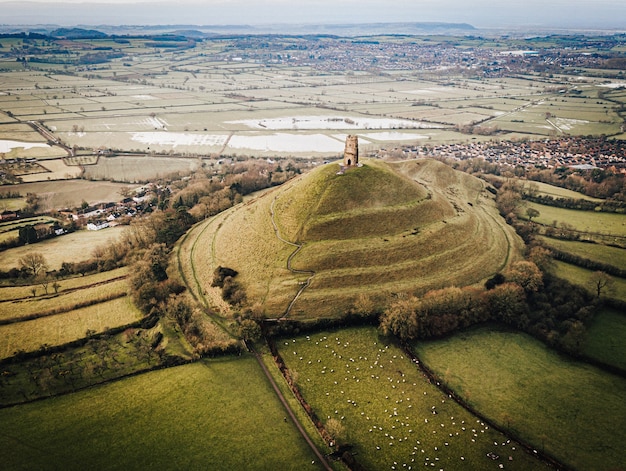 Foto grátis foto aérea de um antigo castelo no topo de uma colina coberta de grama no meio de campos verdes