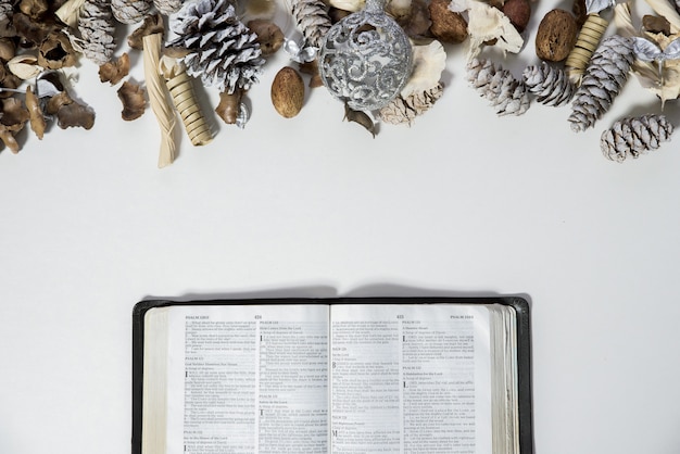 Foto aérea de uma bíblia aberta perto de pinhas e um ornamento em uma superfície branca