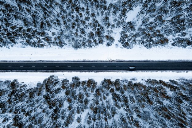 Foto aérea de uma estrada em uma floresta coberta pela neve durante o inverno