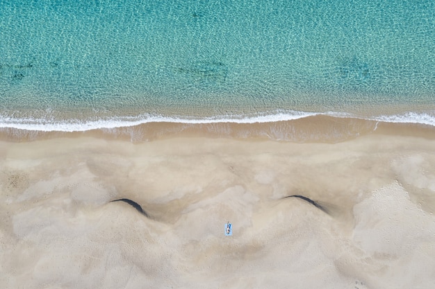 Foto aérea de uma pessoa deitada na praia perto do mar