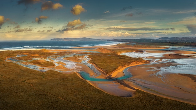 Foto aérea de uma terra cercada pelo mar sob um céu laranja ao pôr do sol