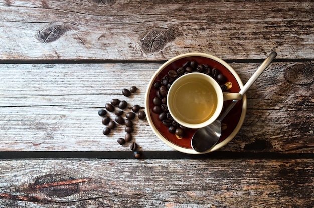Foto aérea de uma xícara de café perto de grãos de café e uma colher de metal numa superfície de madeira