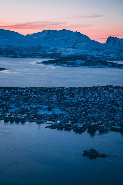 Foto aérea dos edifícios e das montanhas cobertas de neve capturada em Tromso, na Noruega