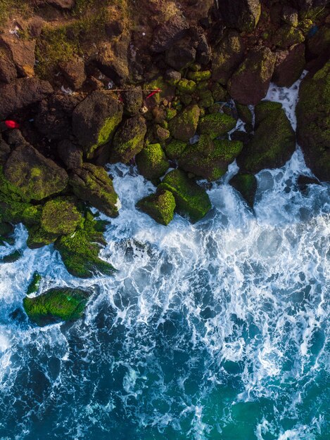 Foto aérea vertical de um mar azul ondulado contra as rochas