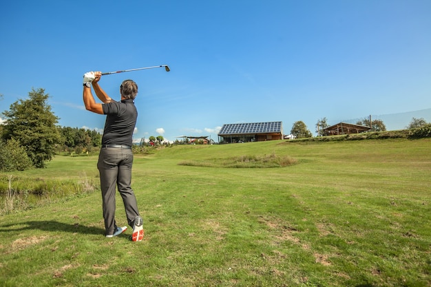 Foto ampla de um atleta masculino balançando um taco de golfe em um dia de sol em um campo de golfe