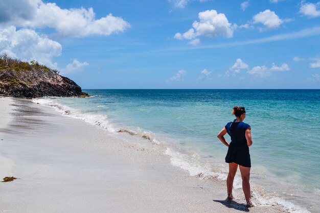 Foto ampla de uma mulher em pé na praia apreciando a vista do oceano