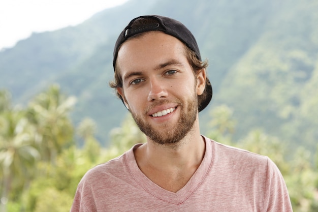 Foto ao ar livre de jovem homem branco com barba relaxando ao ar livre, cercado por um belo cenário de montanha e floresta tropical