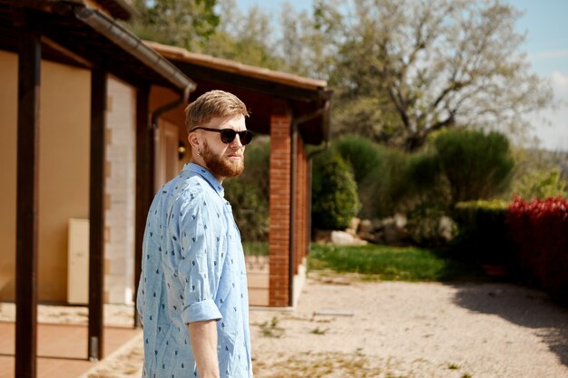 Foto ao ar livre de um jovem europeu elegante e bonito com barba espessa passando um dia ensolarado de verão