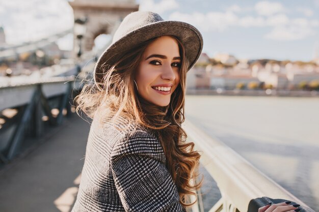 Foto ao ar livre de uma mulher europeia romântica com penteado encaracolado passando um tempo ao ar livre, explorando a cidade europeia