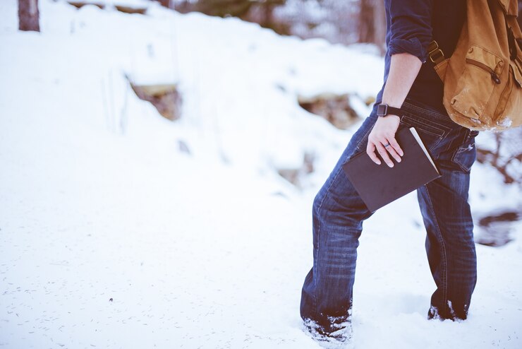 Foto grátis foto aproximada de um homem de pé na neve com uma mochila e segurando a bíblia