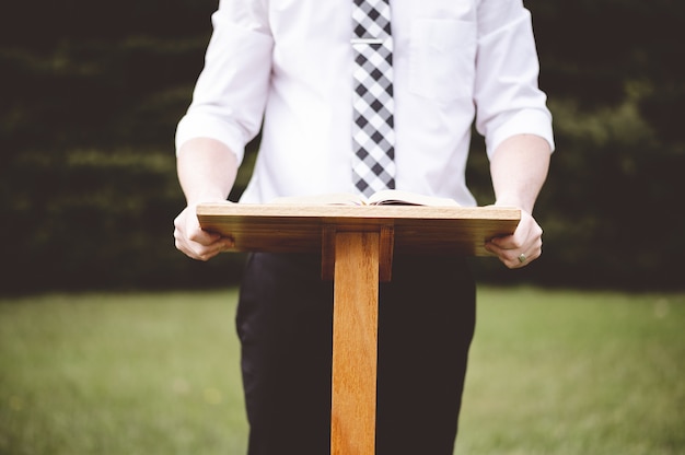 Foto aproximada de um homem em frente a um suporte de discurso com um livro aberto