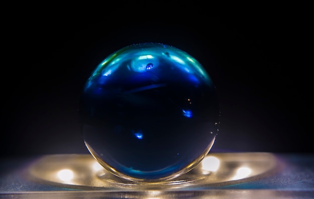 Foto aproximada de uma bola de gude azul escura em cima de uma superfície iluminada com um fundo escuro