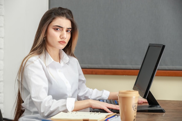 Foto aproximada de uma jovem empresária sentada atrás da mesa e olhando para a câmera