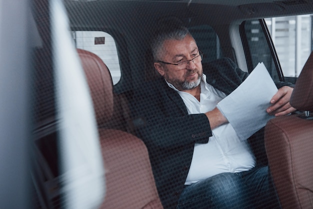 Foto grátis foto através do vidro. papelada no banco de trás do carro. homem de negócios sênior com documentos