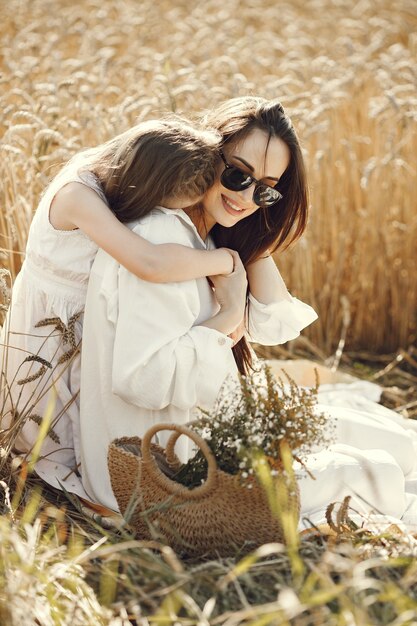 Foto bonita de uma jovem mãe e sua filha em roupas brancas no campo de trigo em um dia ensolarado. Morena mãe e filha posando para uma foto