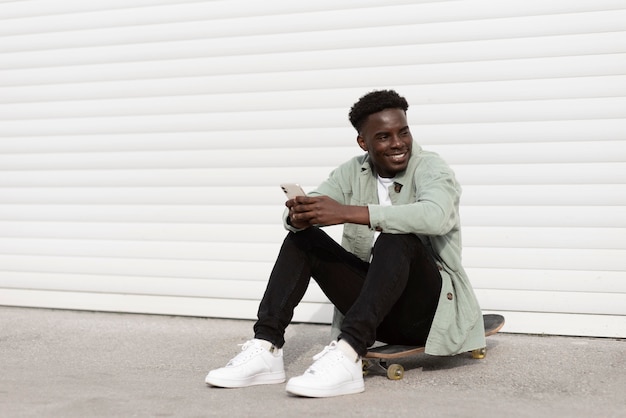 Foto completa adolescente sentada no skate com o telefone